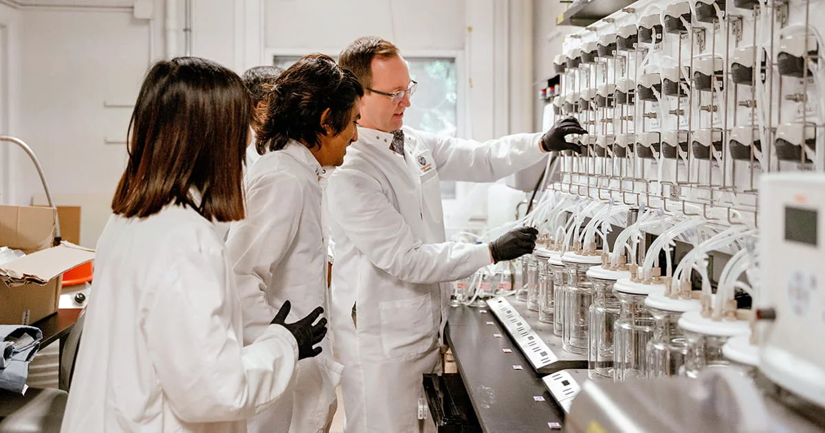 Students observing a researcher work with advanced lab equipment, demonstrating hands-on learning and research opportunities in nutrition science.