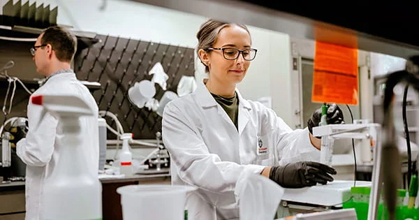 Two researchers in white lab coats working in a scientific laboratory setting with various equipment and containers.