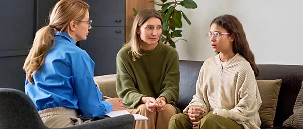 A family counselor meets with a mother and daughter in an office setting.