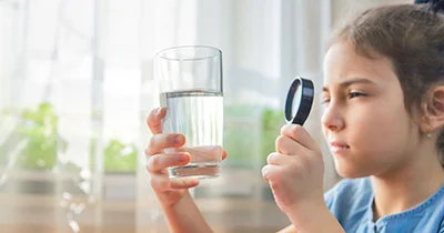 A young girl uses a magnifying glass to look at a glass of water.