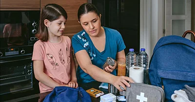 A woman and a young girl are packing an emergency kit together.