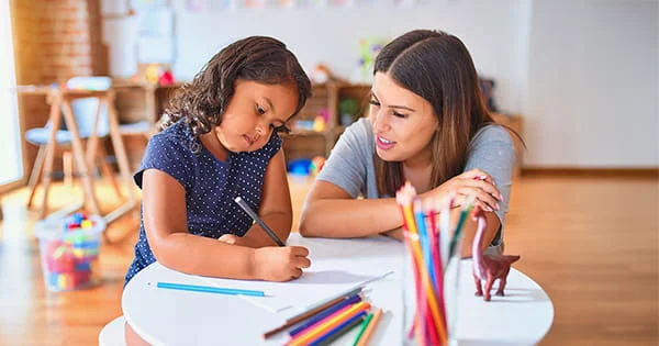An adult interacting with a child as they draw, representing research or learning in a child development setting.