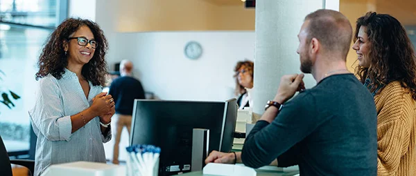 A professional working in health promotion or a service role assists or advises two clients at a desk, illustrating health interaction or patient service.