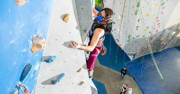 A woman with physiological monitoring equipment climbs a rock wall, illustrating a performance analysis or research study in kinesiology or exercise science.
