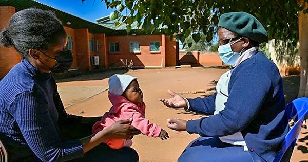 A masked public health worker in Botswana provides counseling to a mother holding her baby, representing maternal and child health services.
