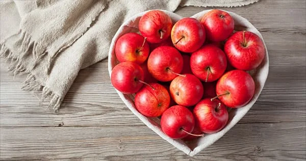 Red apples arranged in a heart-shaped container, symbolizing love for healthy food or appreciation for a nutrition program.