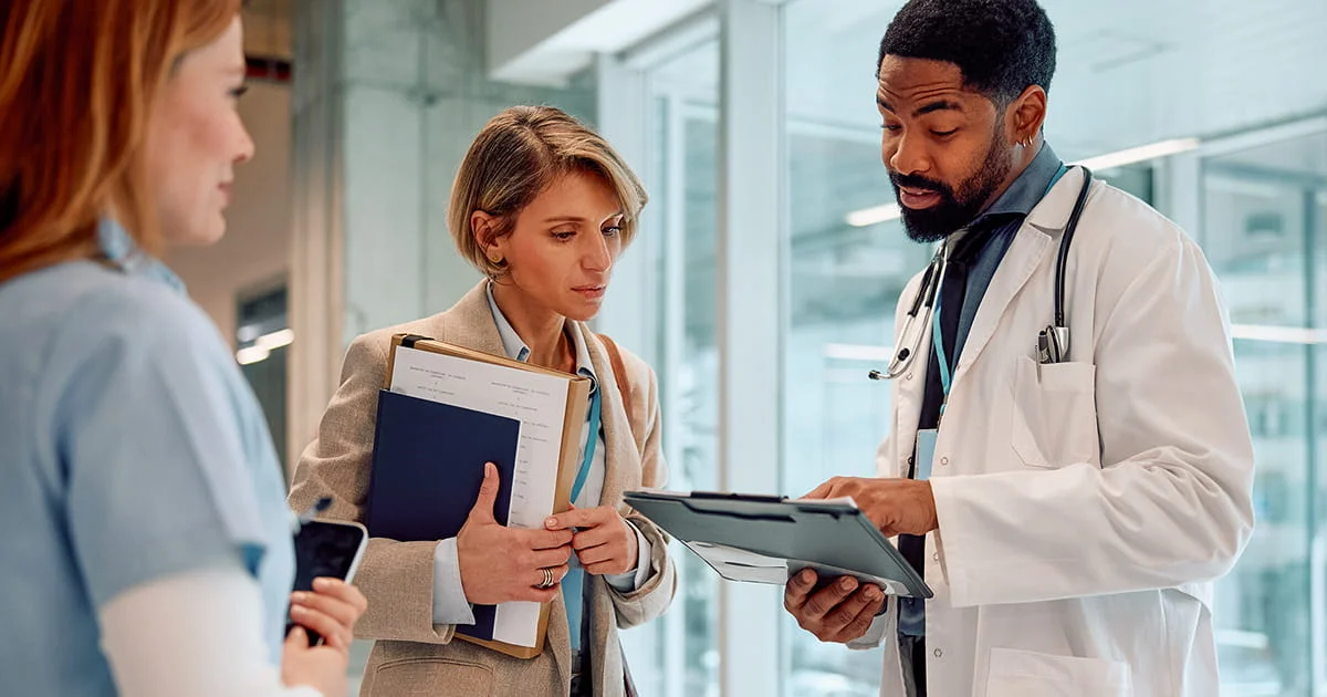 Medical professionals in discussion, holding documents and clipboard in a hospital corridor.