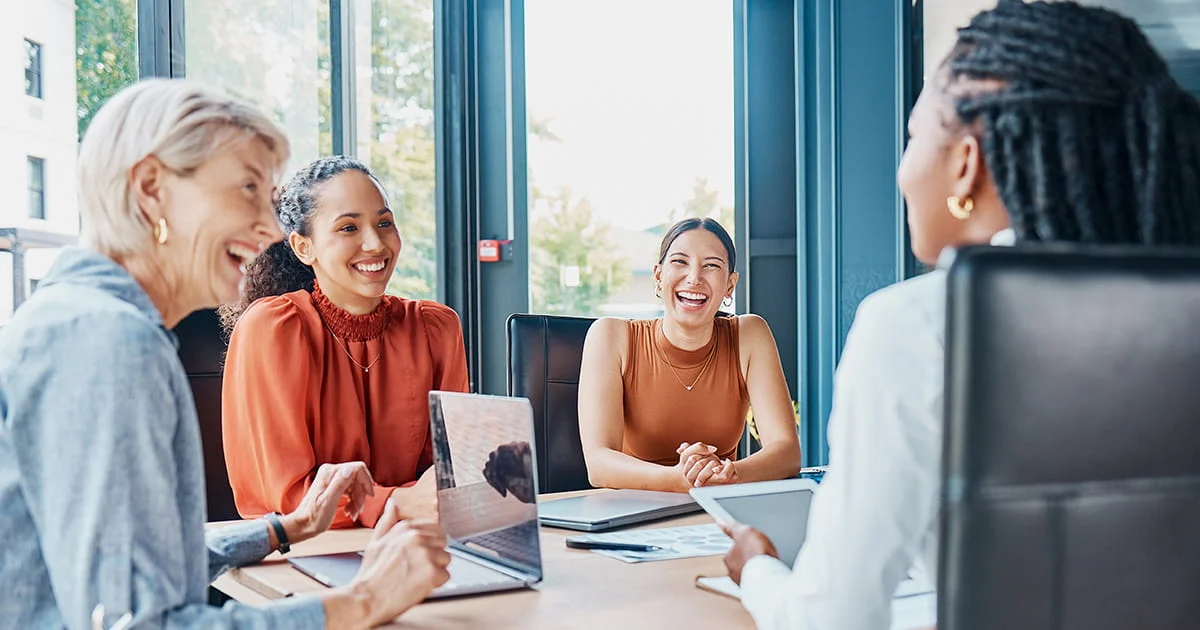 Diverse group of four women collaborating around a table in a modern office, engaged in a lively and cooperative discussion.