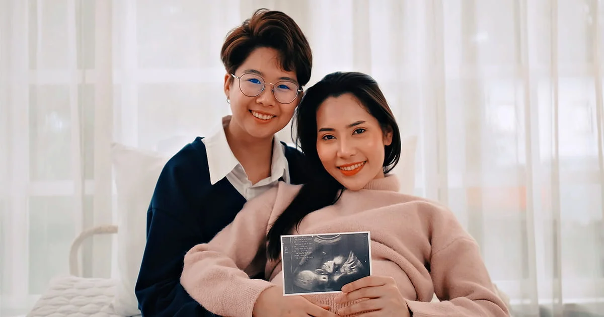 An LGBTQ+ couple smiling and holding a sonogram image, symbolizing family formation and support resources.