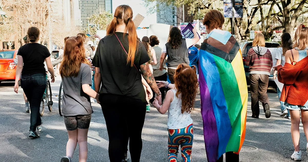 People participating in an LGBTQ+ pride or support march, with families and allies holding hands.