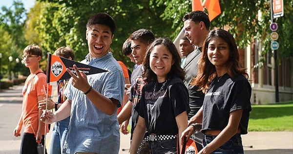 Group of excited college students engaging with an event or parade on campus, illustrating student life and community spirit.