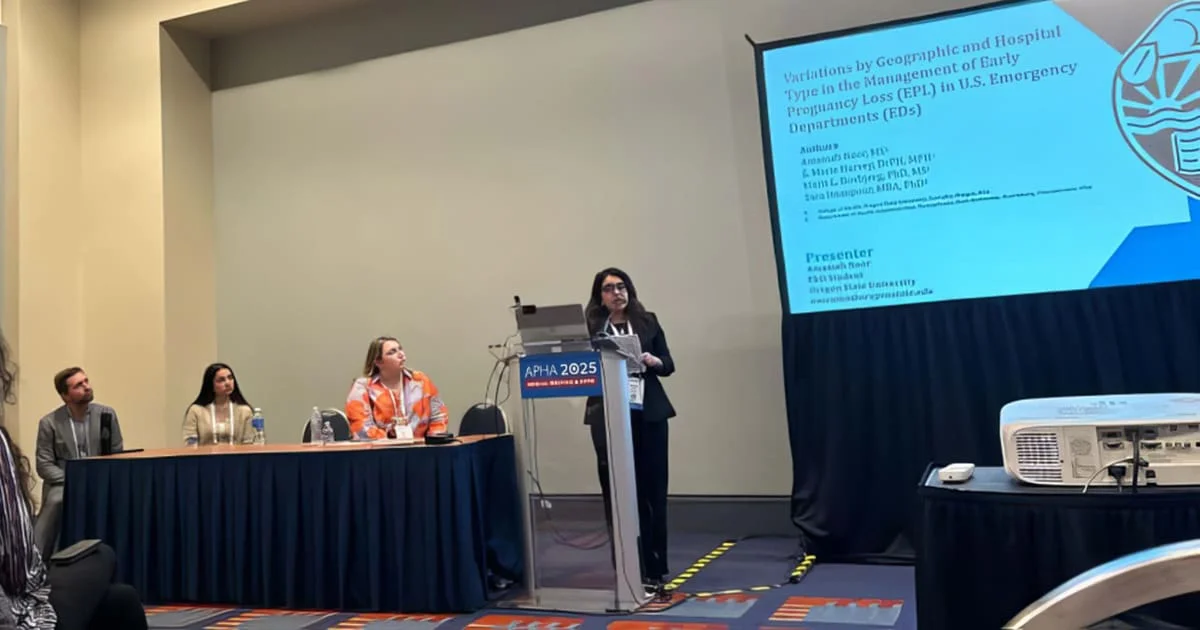 A presenter speaking at a podium during the APHA 2025 conference, with her research title displayed on a screen.