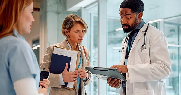 Medical professionals in discussion, holding documents and clipboard in a hospital corridor.