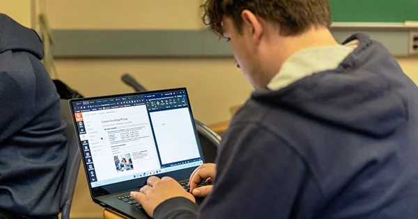Student taking a standardized online test or language placement exam in a classroom setting, utilizing a personal laptop.