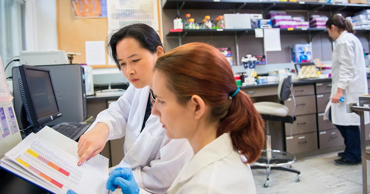 A professor and student collaborating in a research lab, reviewing experiment results and demonstrating scientific mentorship.