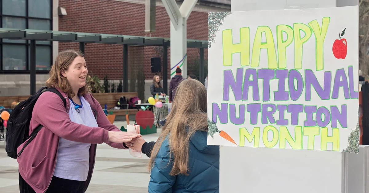 A student volunteer at a booth promoting National Nutrition Month, illustrating community outreach and health education.
