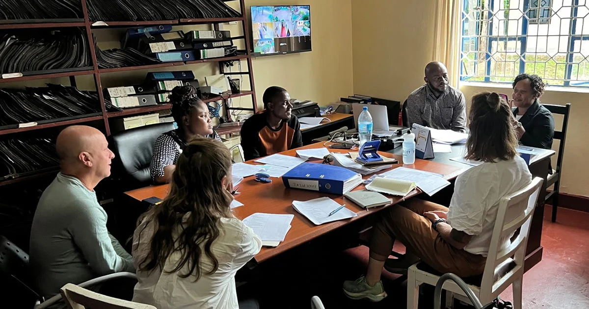 A diverse team of researchers and community partners meeting in an office to discuss project data and collaboration.