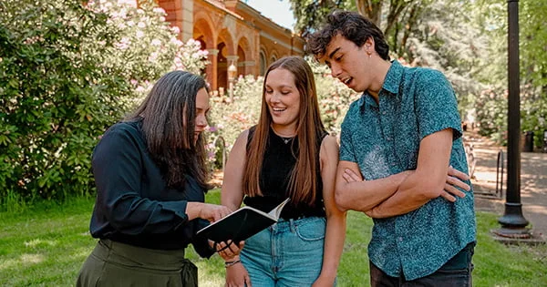 Academic advising session taking place outside a classic university building. A mentor reviews study plans or pathways with two pre-health or pre-med students.