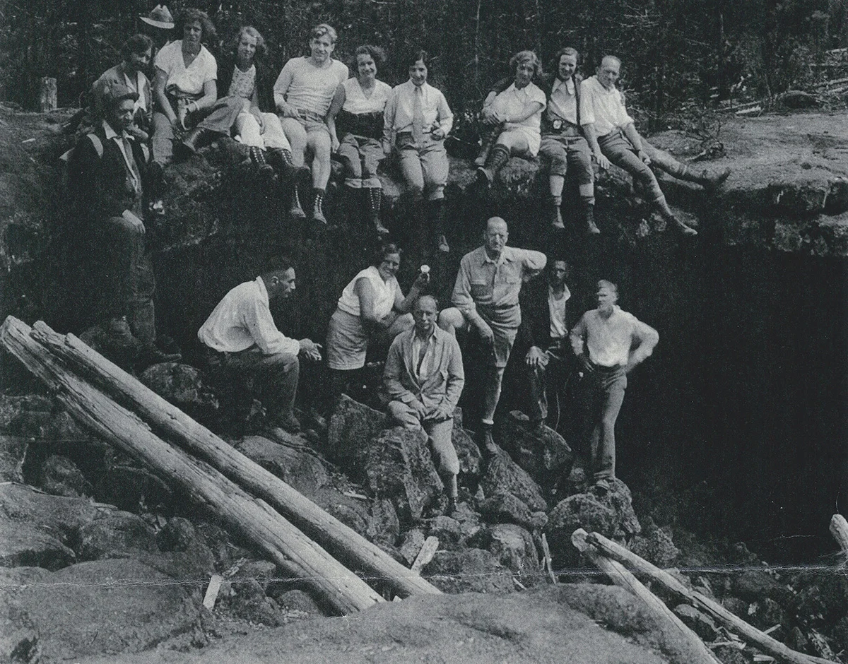 A historic photo showing a group of students and instructors exploring a cave entrance during a geology or field studies trip
