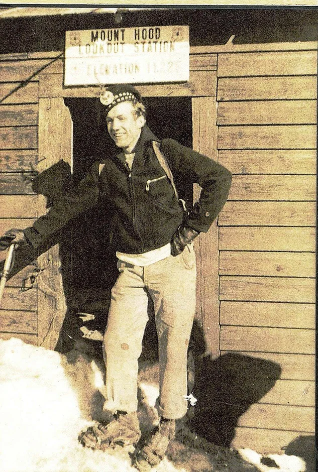 A vintage photograph of an adventurous young man standing at the entrance to the Mount Hood Lookout Station, where a sign lists the elevation as 11,225 feet.
