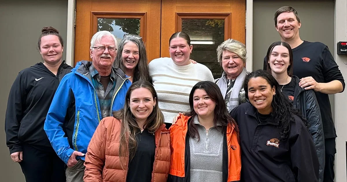 A group of ten diverse individuals of various ages posing for a photo in front of large wooden double doors.