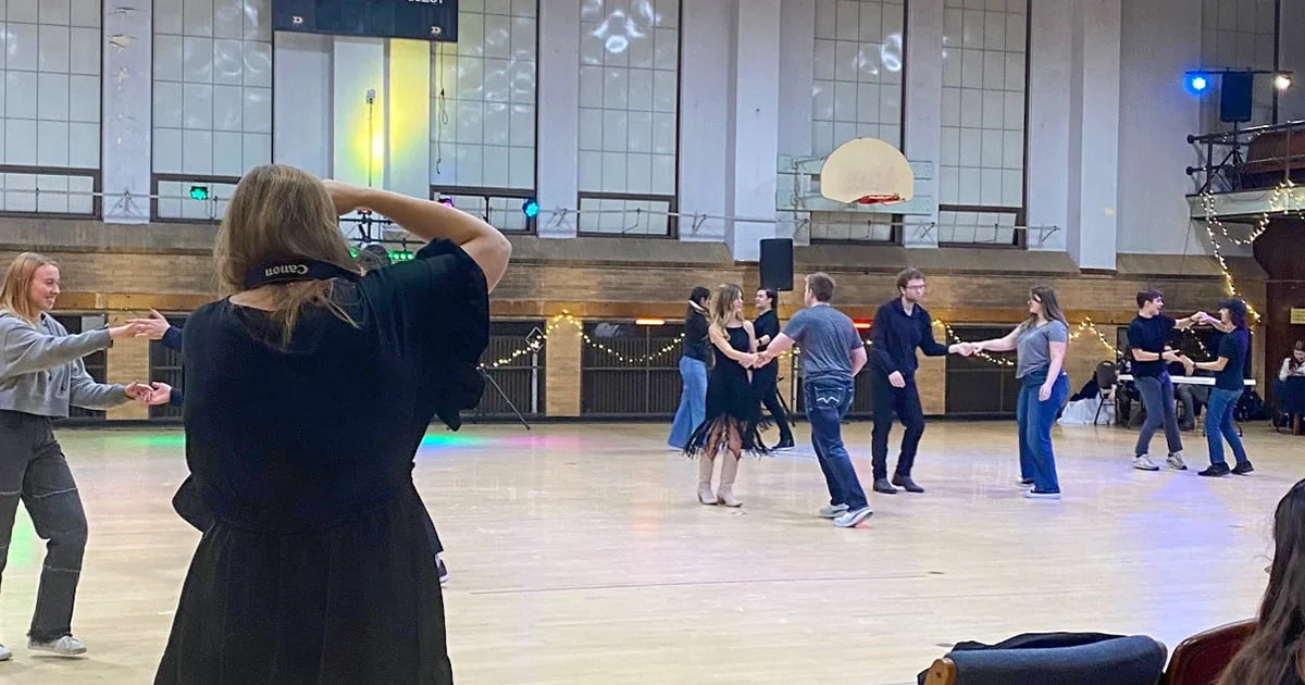 A group of students dances on a large wooden floor during a campus event or club meeting, fostering community and social interaction.