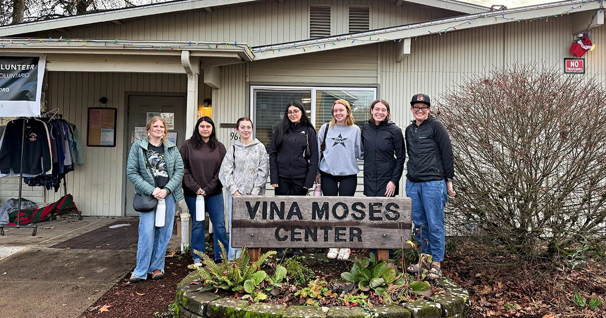 A group of diverse student volunteers poses at the Vina Moses Center, symbolizing community partnership and service learning.