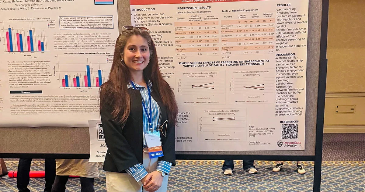 A smiling woman with long brown hair stands in front of her academic research poster titled, "Effects of Parenting on Engagement at Varying Levels of Family-Teacher Relationships."