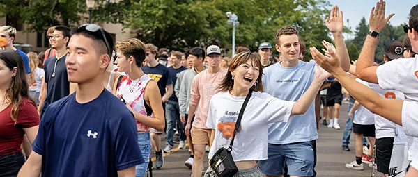 Students smiling and waving in a large crowd, representing a vibrant and engaged campus community.