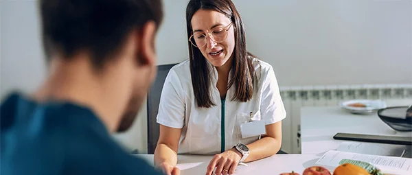 A student or practitioner in a Dietetics program counseling a client. Fresh fruit is visible on the desk, emphasizing health and nutrition advice.
