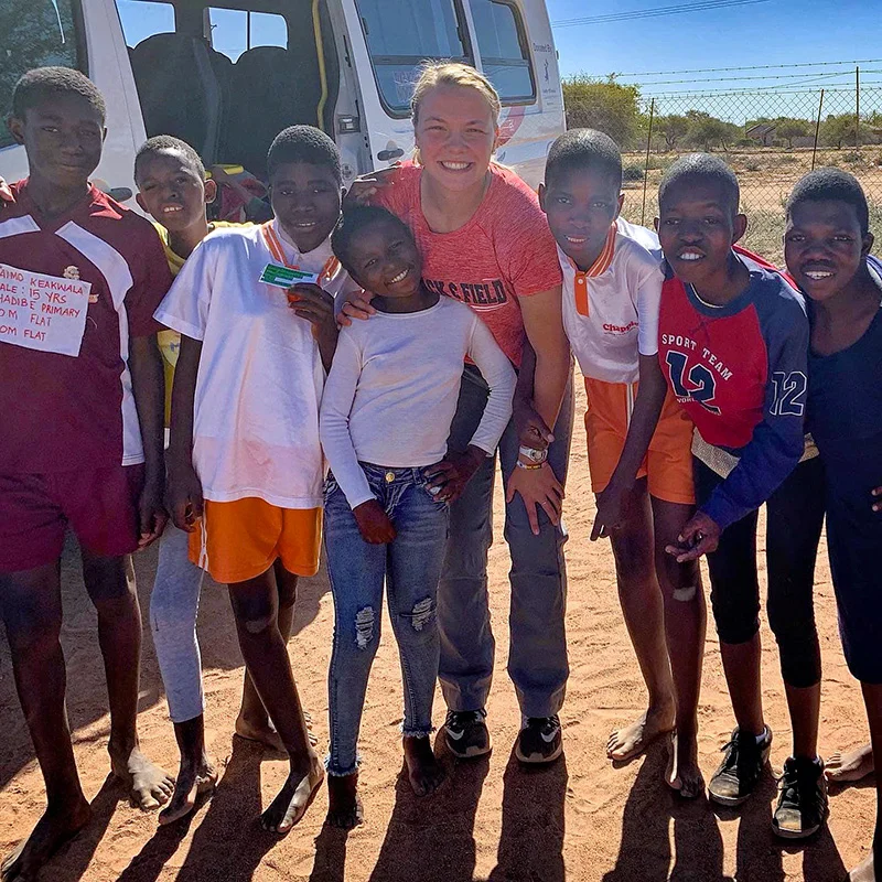 A student researcher poses happily with local children in Botswana during a research trip, symbolizing global outreach and community partnership.