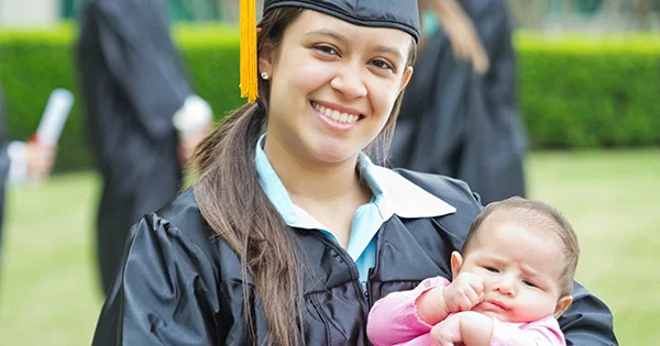 A student parent celebrating graduation while holding her baby, illustrating the impact of child care assistance programs on academic success.