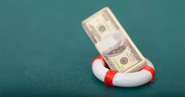 A stack of cash inside a miniature life preserver, symbolizing emergency financial assistance, rescue loans, and economic lifelines for those in need.