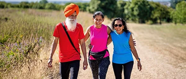 Outdoor portrait of a Sikh man with a long white beard, and two women walking together on a nature trail on a sunny day.