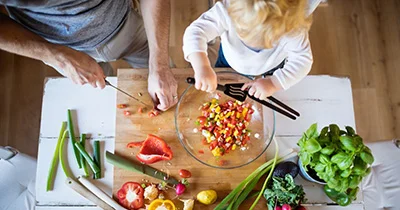 Father and child making salad together. Illustrates healthy eating habits and family time in the kitchen.