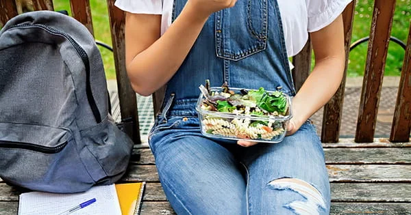 Student on a bench enjoying a healthy salad. Backpack and books suggest a break from studying.