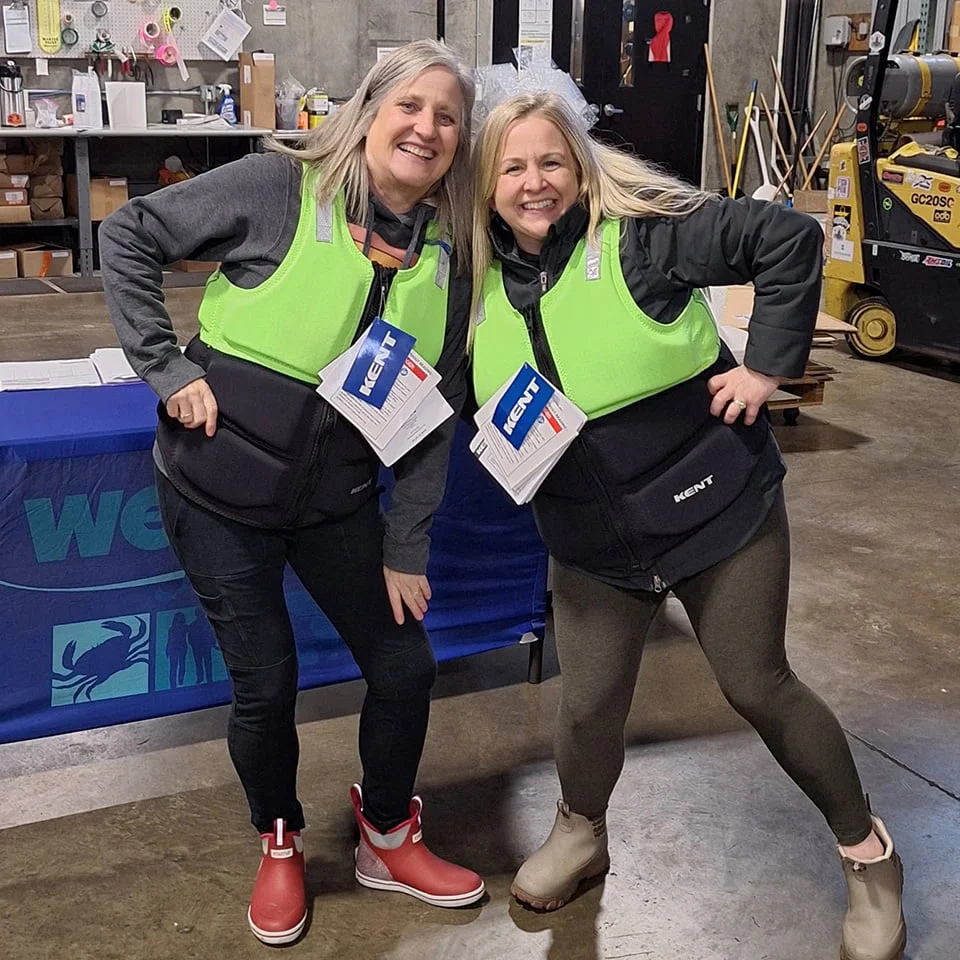 Two smiling volunteers in "KENT" life vests promote water safety, holding informational brochures at a community event.