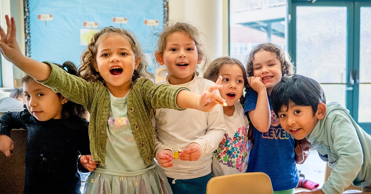 A diverse group of young students expressing excitement and joy in a vibrant classroom environment.