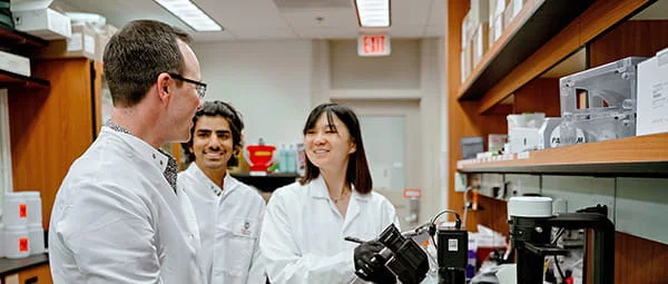 Diverse researchers smiling and discussing findings while working with an inverted microscope in a professional laboratory setting.