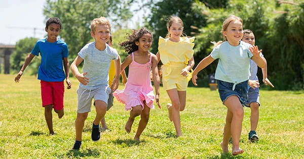 Happy children of various backgrounds enjoying outdoor play and physical activity in a bright park setting.