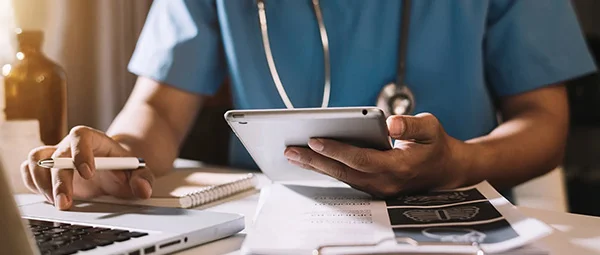 Clinician utilizing digital tools and printed medical records to streamline patient care and data management.