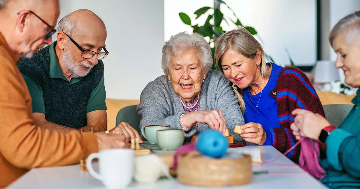 Senior citizens socializing and participating in mentally stimulating leisure activities together in a bright, indoor communal setting.