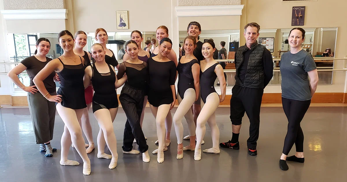 Ballet students and instructors posing together for a group portrait in a professional dance studio setting.