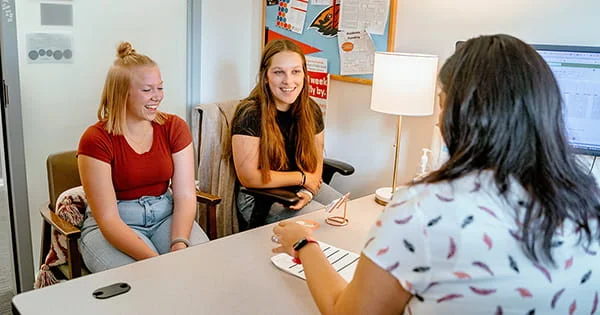 Students sharing a laugh during an academic advising session with a staff member in a university office.
