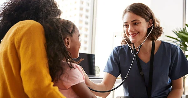 A young child receives a pediatric checkup from a friendly healthcare professional using a stethoscope.