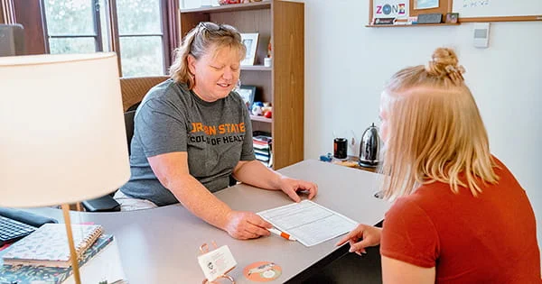 Academic advising session where an advisor in an Oregon State t-shirt reviews paperwork with a student in a bright office.