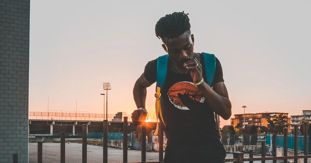 A person with a backpack standing in front of a building at sunset.