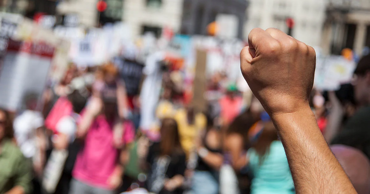 A raised fist over a crowd of demonstrators, symbolizing social justice, activism, and resistance.
