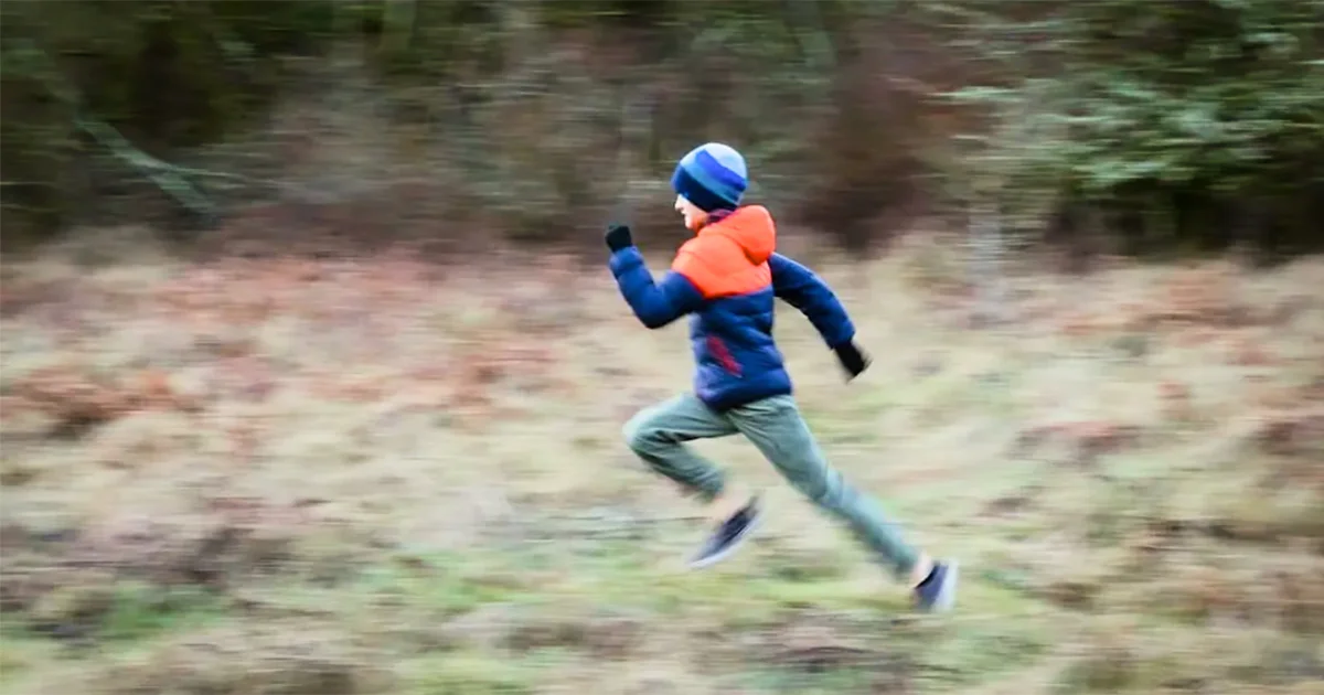 A child vigorously runs through a forest clearing, symbolizing active outdoor play, physical health, or energy.