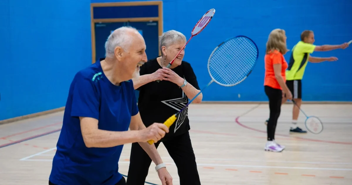 Active seniors participating in a recreational indoor badminton match, promoting community fitness and social engagement.